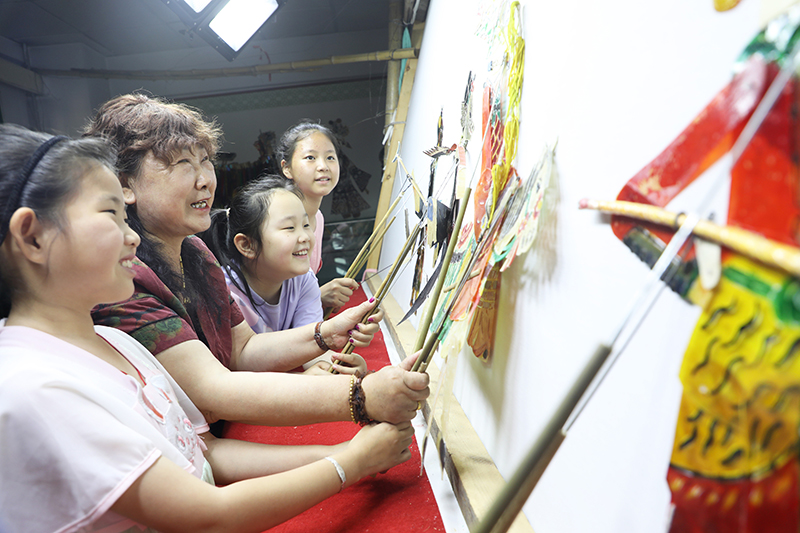 皮影藝人指導小朋友表演皮影戲。